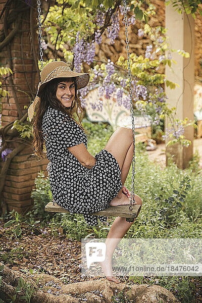 Smiling young woman sitting on tree swing in backyard