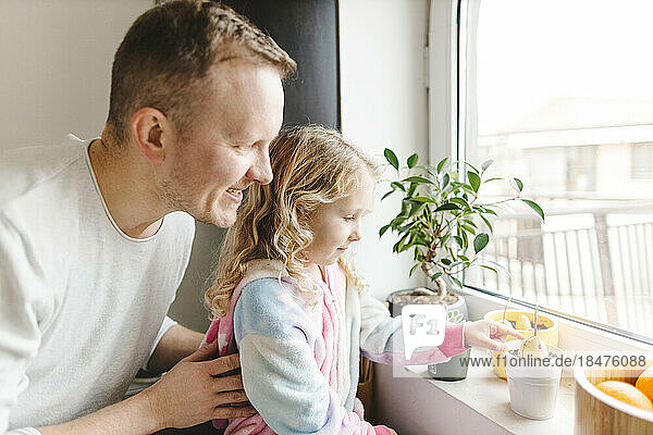 Glücklicher Vater und Tochter kümmern sich zu Hause um Pflanzen auf der Fensterbank