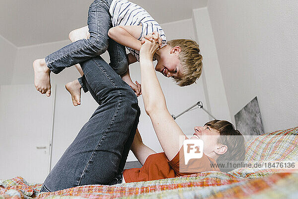 Son playing with mother lying on bed at home