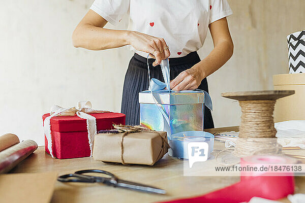 Woman tying ribbon on gift box at desk