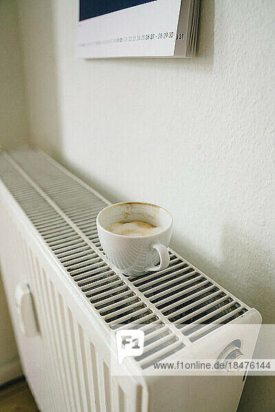 Cup of coffee kept on radiator near wall at home