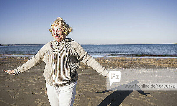 Smiling elderly woman with arms outstretched in front of sea