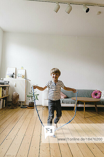 Smiling boy practicing jumping rope in living room at home