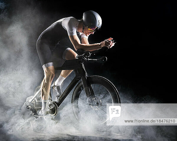 Cyclist wearing sports clothing sitting on turbo trainer against black background