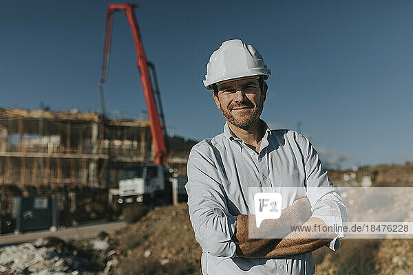 Lächelnder reifer Architekt mit Schutzhelm steht auf der Baustelle
