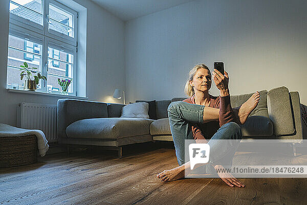 Mature woman using smart phone and practicing yoga at home