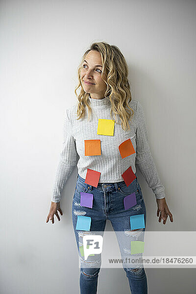 Thoughtful woman with colorful adhesive notes on body near wall