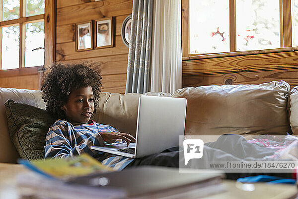 Boy using laptop resting on sofa at home