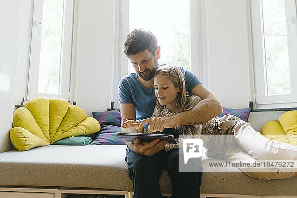 Father using tablet PC with daughter sitting on seat at home