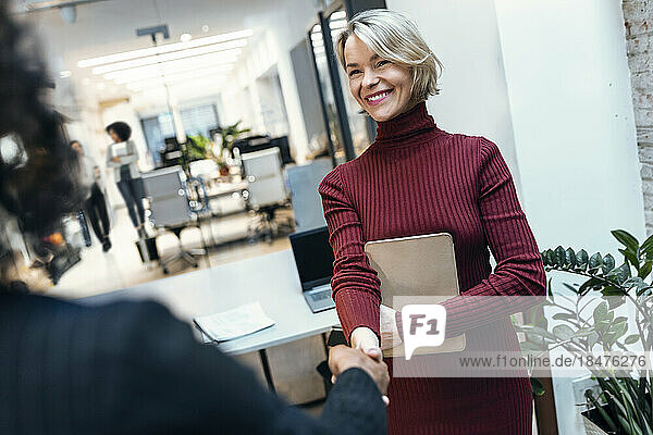 Happy businesswoman shaking hand with colleague at workplace