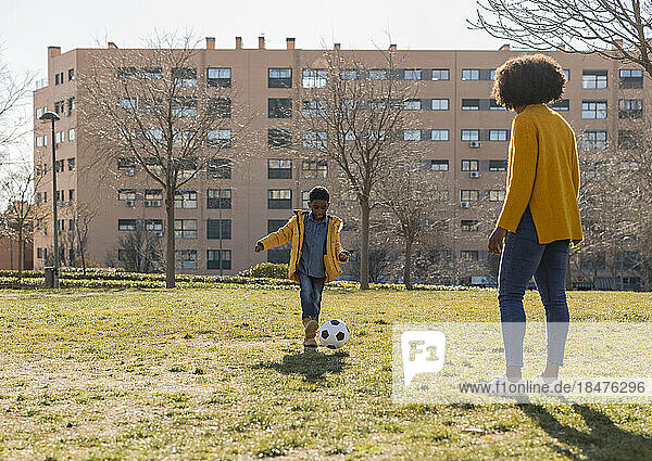 Junge spielt an sonnigem Tag mit Mutter im Park Fußball