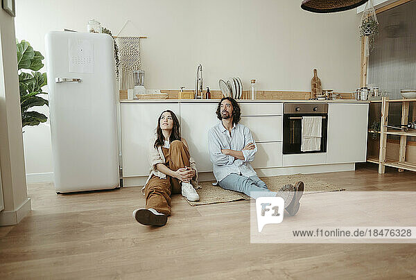 Contemplative couple sitting in front of cabinet at kitchen