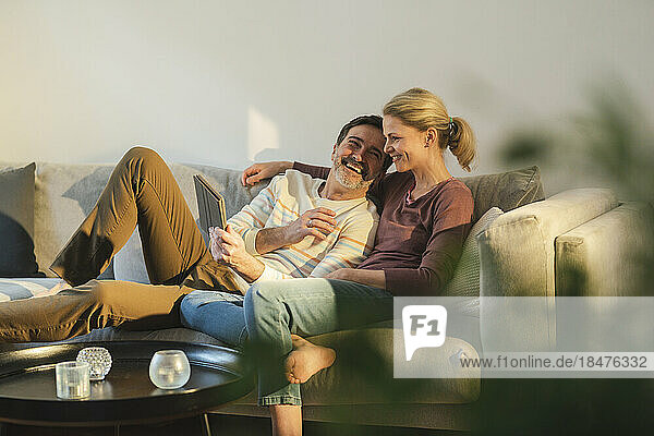 Happy man holding tablet PC enjoying with wife on sofa at home