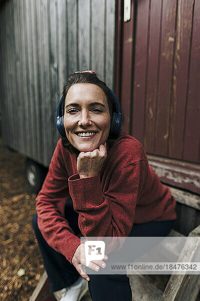 Happy woman wearing wireless headphones sitting in front of door