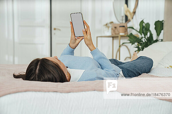 Young woman using mobile phone lying on bed at home