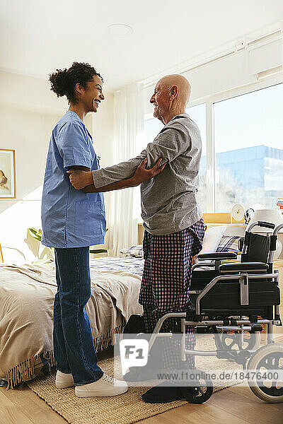 Physiotherapist assisting senior man in standing at home