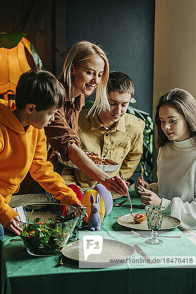 Happy woman serving food to family having Easter dinner at home