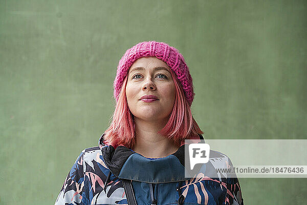 Thoughtful woman wearing knit hat in front of green wall