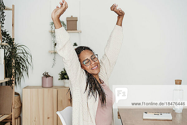 Smiling freelancer with eyes closed stretching arms at desk