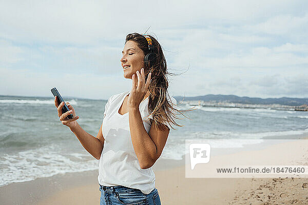 Frau genießt es  am Strand Musik über Smartphone und Kopfhörer zu hören
