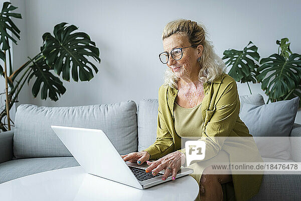 Happy elderly freelancer working on laptop sitting at home