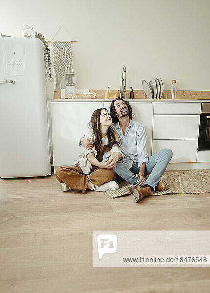 Glückliches Paar sitzt mit gekreuzten Beinen auf dem Boden und träumt in der Küche
