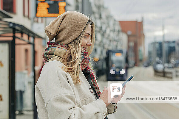 Smiling woman text messaging through smart phone at street