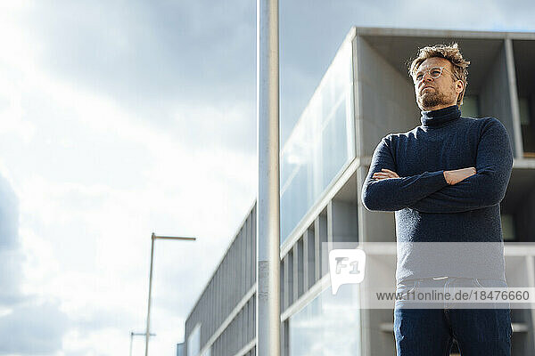 Businessman contemplating with arms crossed in front of modern office building