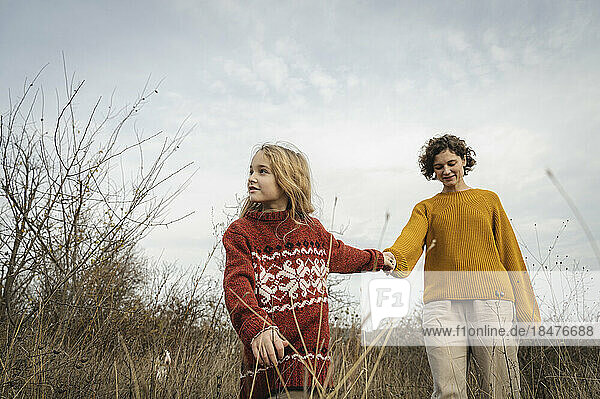 Thoughtful daughter holding hands of mother under sky