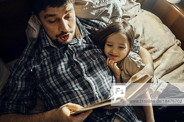 Father reading story book lying with son on bed