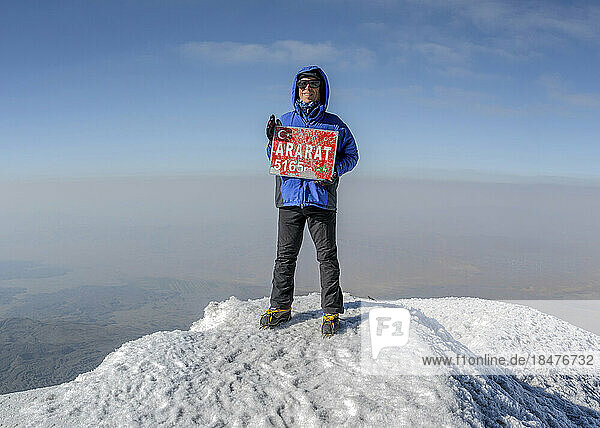 Smiling hiker with signboard on Mt Ararat peak at sunny day