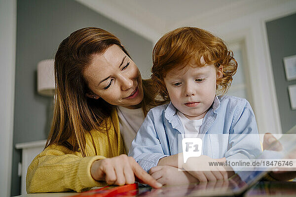 Mother assisting son reading book at home
