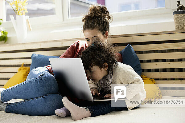 Kleines Mädchen sitzt mit Laptop auf dem Schoß der Mutter auf der Couch zu Hause