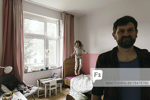 Mature man with daughter jumping on bed in background