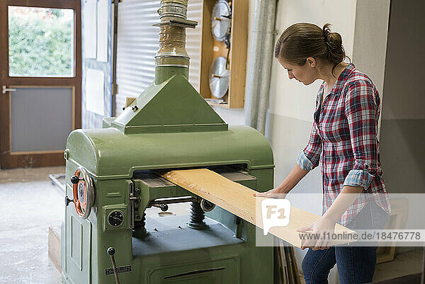 Craftswoman cutting plank through machine in woodshop