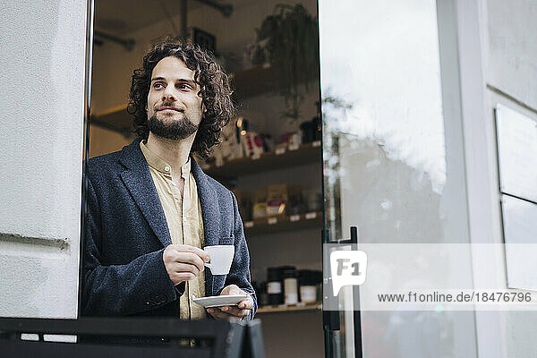 Contemplative businessman with coffee cup standing at doorway