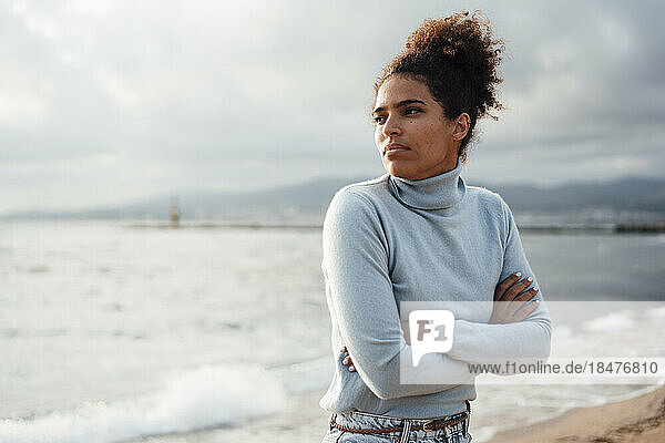 Thoughtful young woman with arms crossed at beach
