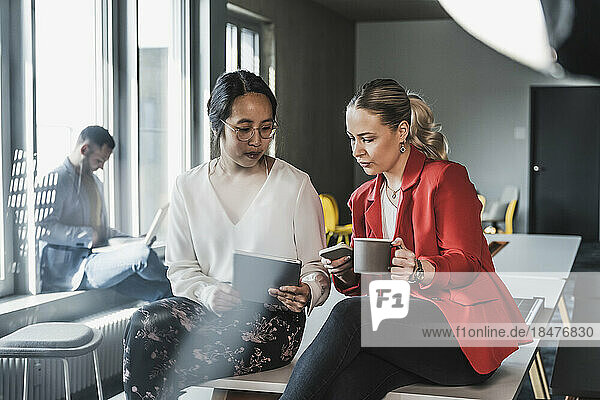 Businesswomen using wireless technologies sitting at desk in office