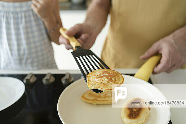 Hand of grandfather flipping pancake using spatula in kitchen at home