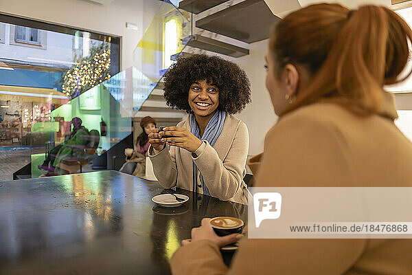 Happy woman holding coffee cup and talking to friend in cafe