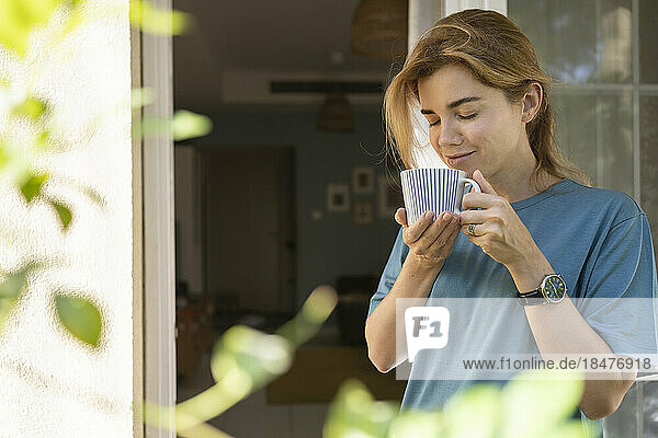 Lächelnde Frau mit Kaffeetasse steht vor der Tür