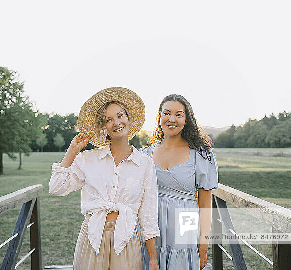 Smiling woman wearing hat standing with friend by railings