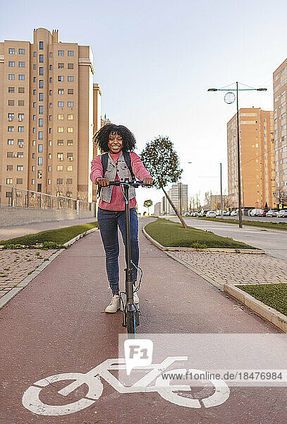 Happy woman with electric push scooter on footpath