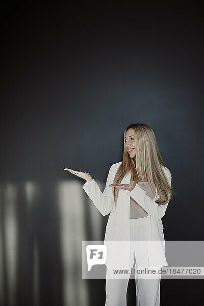 Smiling woman gesturing while standing in front of black wall