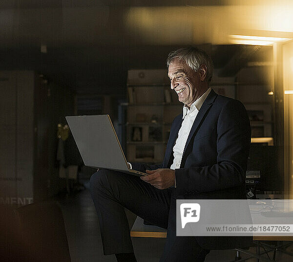 Glücklicher Geschäftsmann mit Laptop  der im Büro sitzt