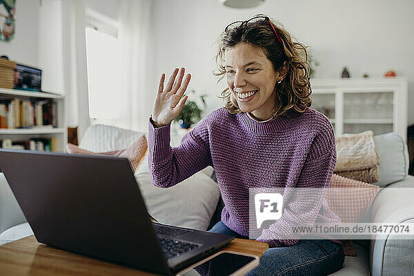 Glückliche Frau winkt zu Hause per Videoanruf über Laptop