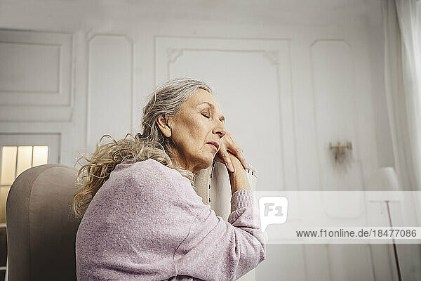 Senior woman with eyes closed sitting on chair at home