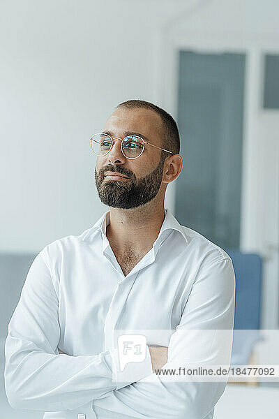 Thoughtful businessman with arms crossed standing at home office