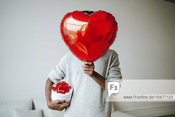 Man covering face with heart shape balloon at home