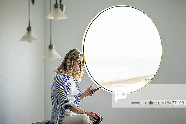 Geschäftsfrau sitzt am Fenster und benutzt Smartphone